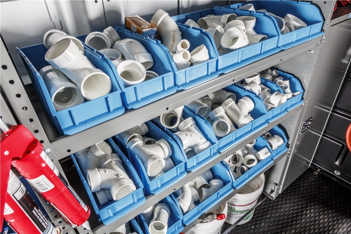 Interior of a commercial van upfitted for plumbing trades with heavy-duty metal shelving and specialized tank storage.